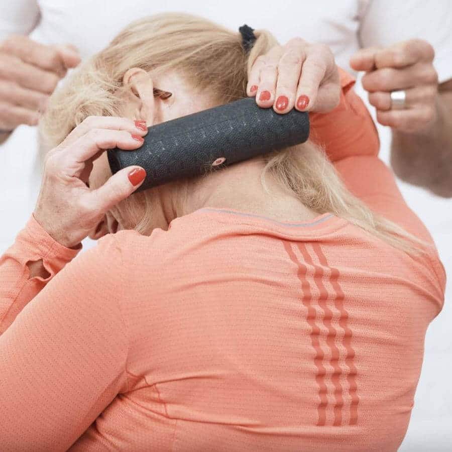 A woman is using a fascia-fit foam roller for her neck.