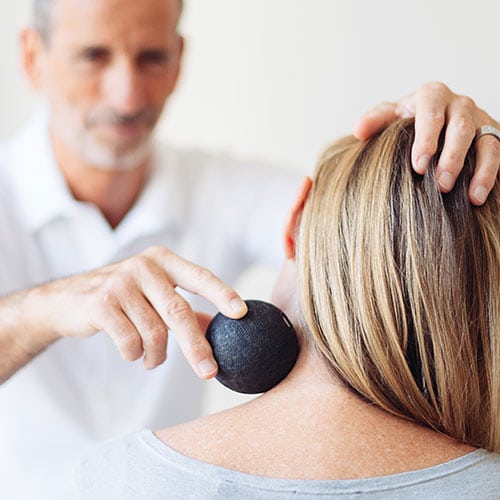 Roland Liebscher-Bracht treating a patient's neck with a massage ball.