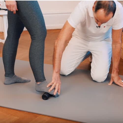 A woman is standing on a fascia roll with her foot.