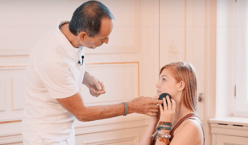 Roland Liebscher-Bracht instructs a girl to roll her cheek with a mini massage ball.