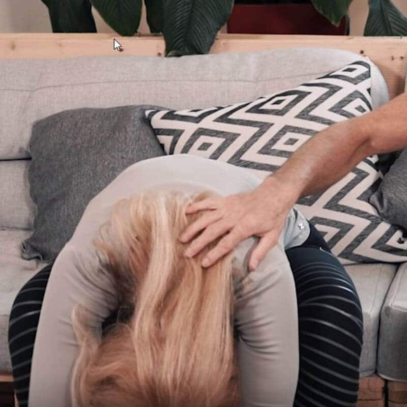 A woman is bending down while sitting on a couch to relieve her heartburn.