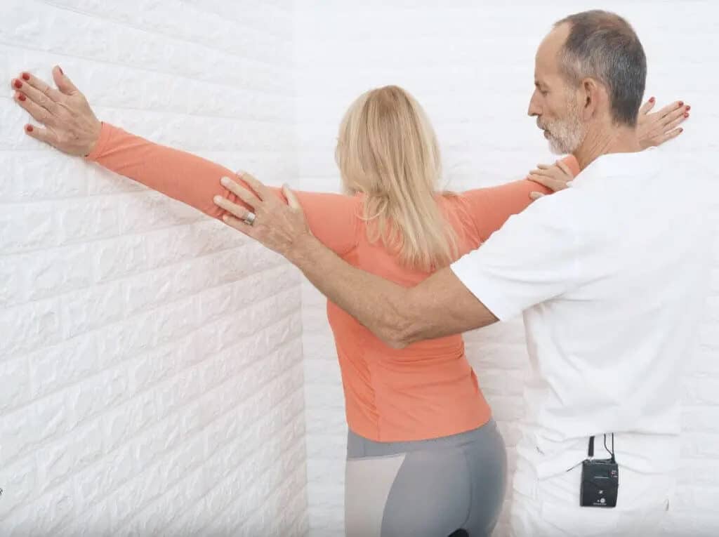 A woman is facing the corner of a wall and stretches out her arms to either side of the wall.
