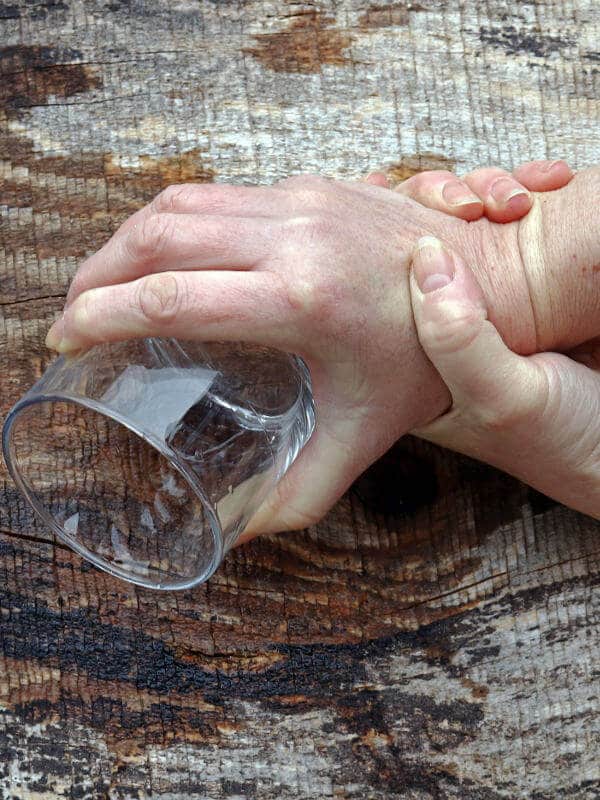 A hand gripping a glass. Another hand grips the wrist of the hand holding the glass.