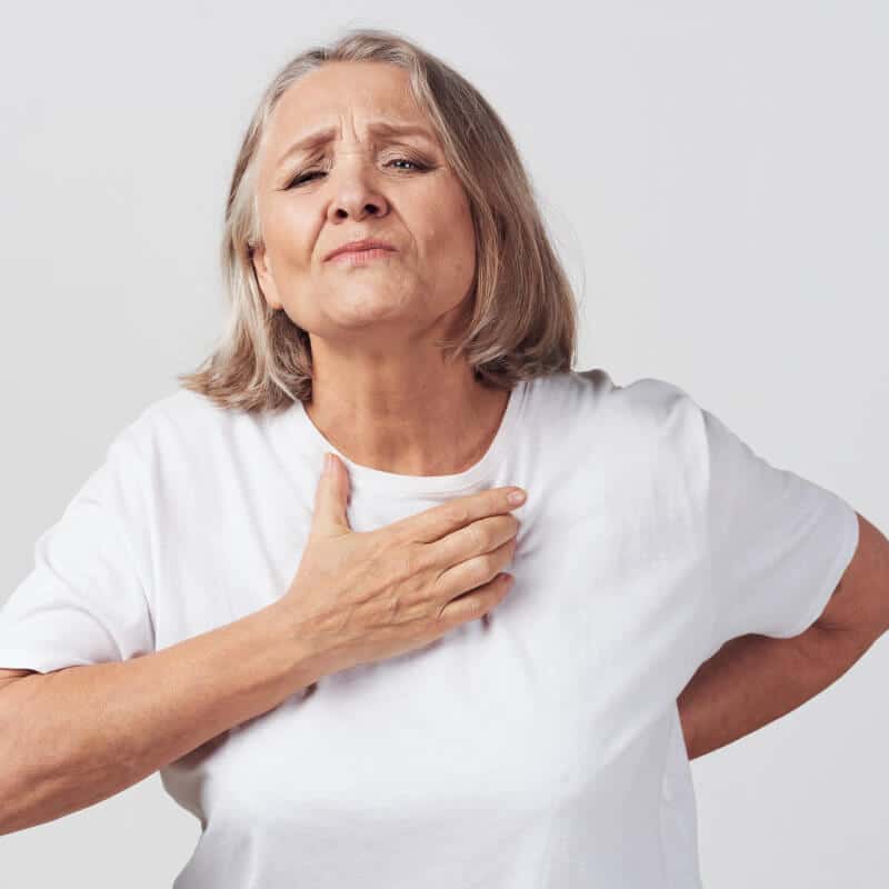 An elderly woman clutches her back and chest area in discomfort.
