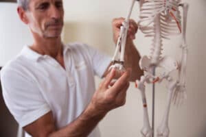 Roland Liebscher-Bracht is holding the arm of a skeleton to show how to treat carpal tunnel syndrome.