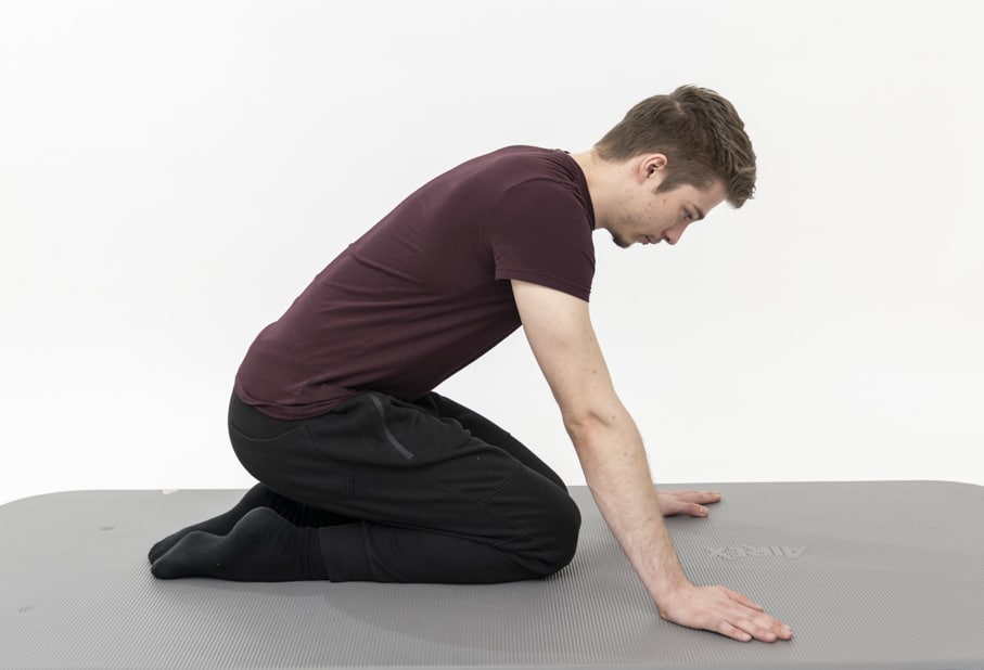 A man sits on his knees and holds his arms straight in front of him, slightly leaning forward.