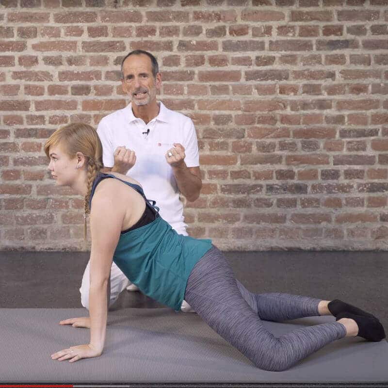 A woman is kneeling on a mat, her arms stretched out and her legs forming a diamond.