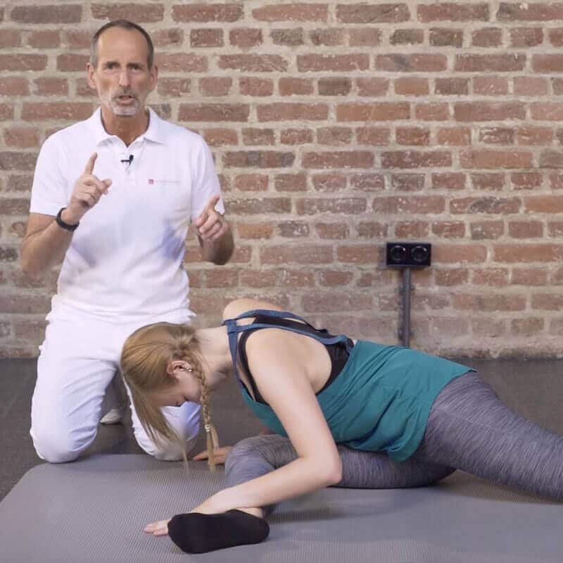 A woman is sitting on a mat, stretching her pelvis.