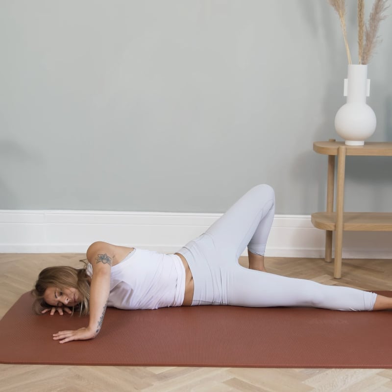 A girl is laying on the floor stretching the left side of her body.