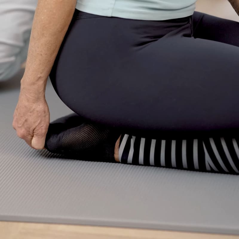 A woman is sitting back on her heels pulling the toes of her right foot upward.