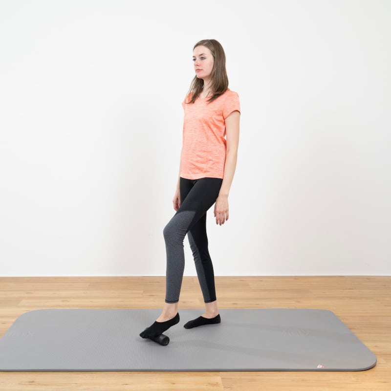 A woman is standing with the mini foam roller under her left foot.