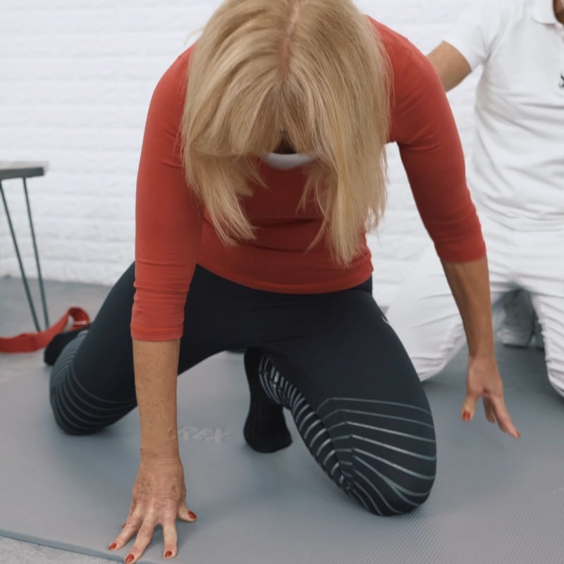 A woman is on her hands and knees stretching the ball of her left foot..