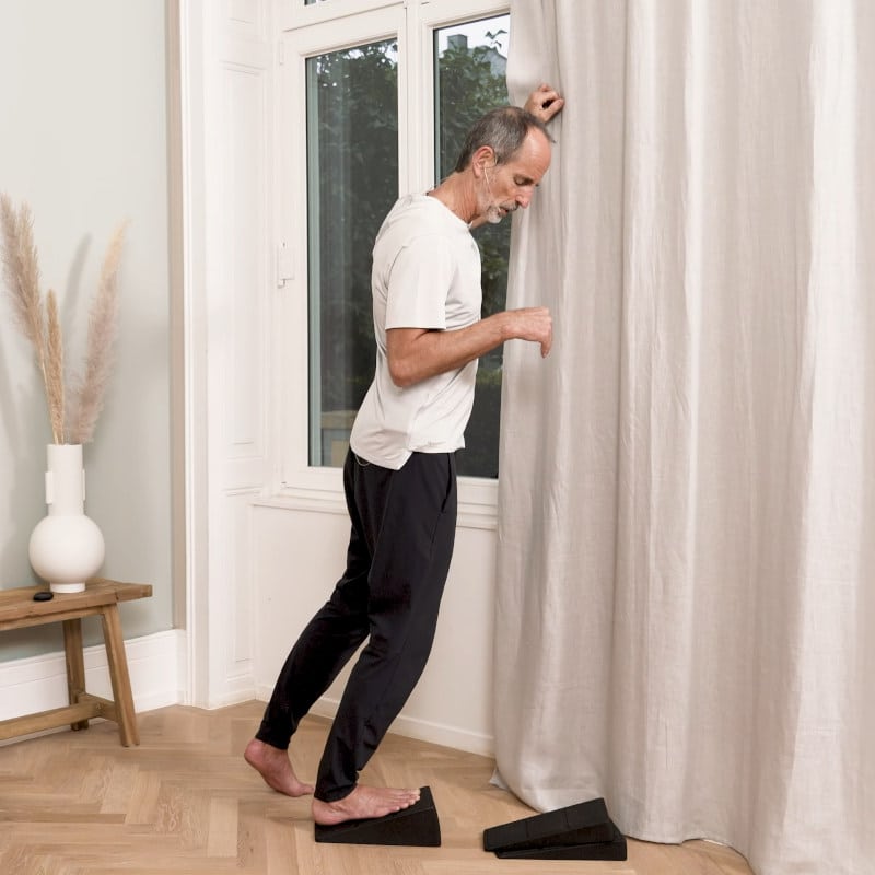 Roland Liebscher-Bracht is standing on the Knee Hero stretching his Achilles'.