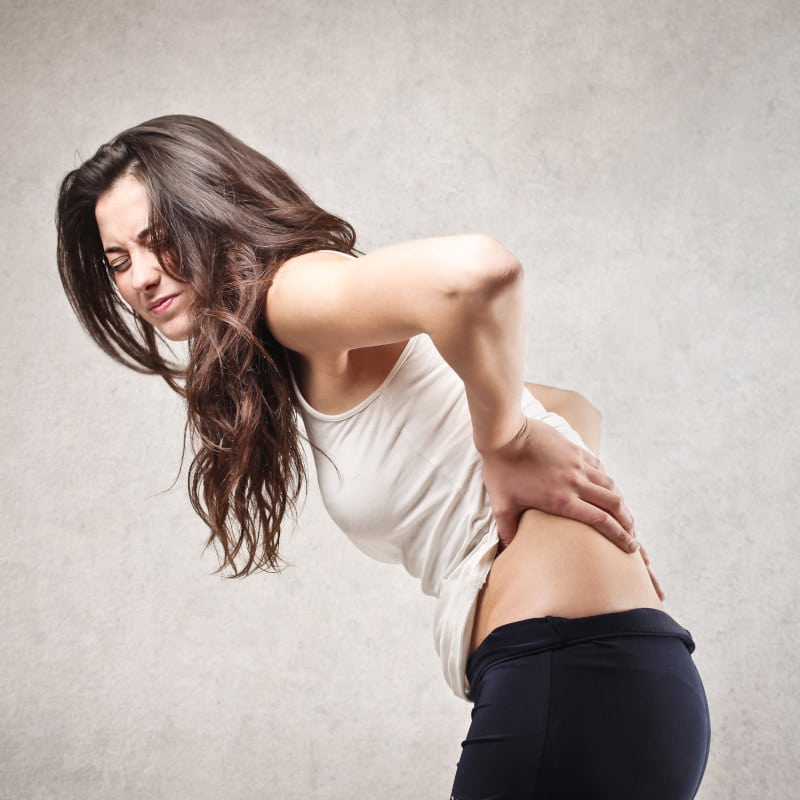 Closeup of a young woman touching her lower back.
