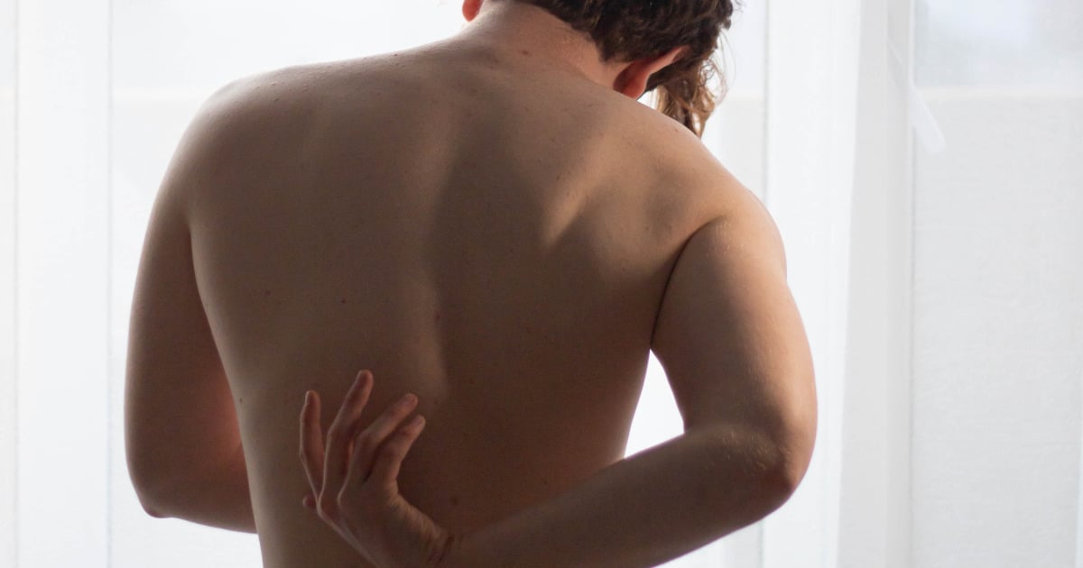 Image of a man's back, he's touching the bottom of his left shoulder blade.