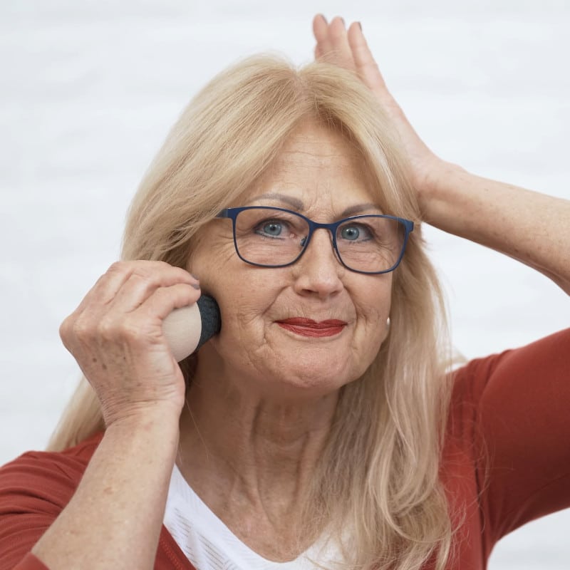 A woman is pressing the Osteopressure tool into her jaw.