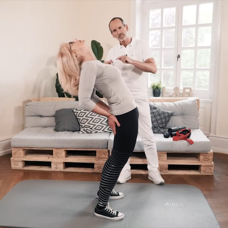 A woman is stretching her hip flexors while Roland Liebscher-Bracht looks on.