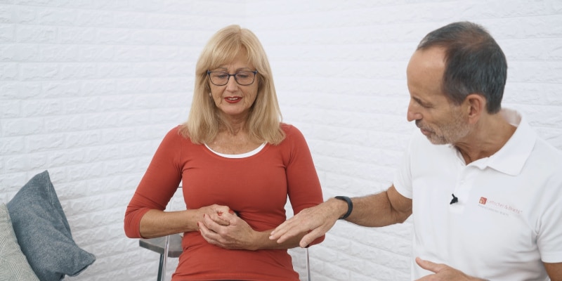 A woman is pressing the Osteopressure tool against her chest while Roland Liebscher-Bracht looks on.
