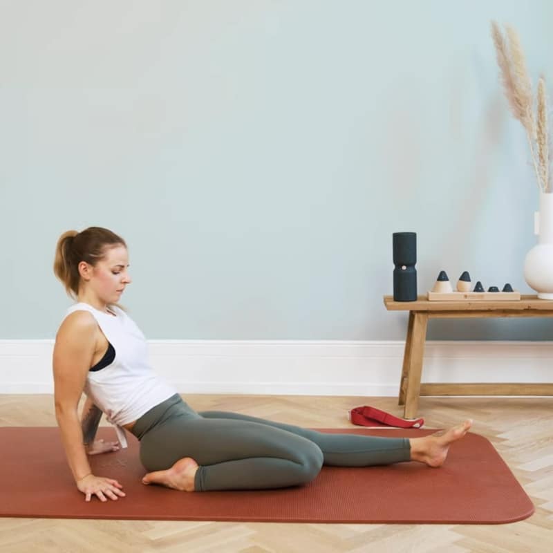 A woman is sitting on the floor with her left leg extended and her right foot next to her buttock.